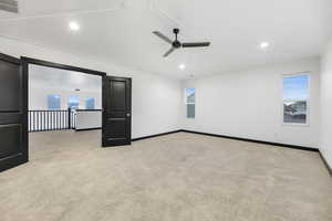 Carpeted empty room featuring ceiling fan, vaulted ceiling, and a wealth of natural light