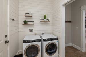 Washroom with wooden walls, washer and clothes dryer, and dark wood-type flooring