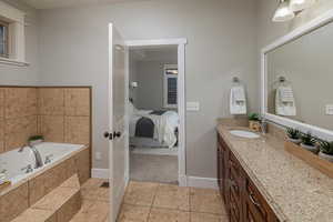 Bathroom with a relaxing tiled tub, vanity, and tile patterned flooring