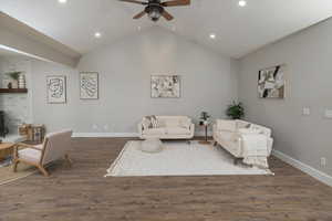 Living room featuring lofted ceiling, ceiling fan, dark wood-type flooring, and a wood stove