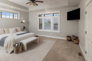 Bedroom with a tray ceiling, light carpet, and ceiling fan