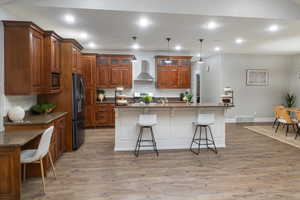 Kitchen with a kitchen island with sink, a kitchen breakfast bar, pendant lighting, and wall chimney range hood