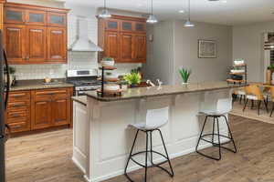 Kitchen featuring a breakfast bar area, wall chimney range hood, and an island with sink