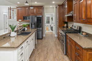 Kitchen featuring light stone counters, white cabinets, hanging light fixtures, light hardwood / wood-style flooring, and appliances with stainless steel finishes