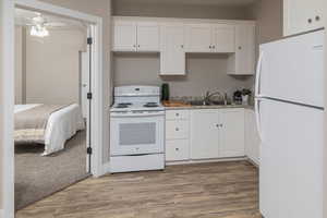 Kitchen featuring white cabinets, hardwood / wood-style flooring, sink, and white appliances