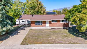 Ranch-style house with a front yard, a mountain view, solar panels, and covered porch