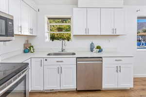 Kitchen with stainless steel appliances, white cabinets, light wood-type flooring, and sink