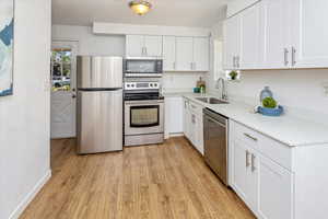 Kitchen featuring light stone counters, sink, white cabinetry, light hardwood / wood-style flooring, and stainless steel appliances