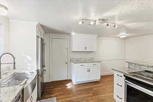 Kitchen featuring dark wood-type flooring, white cabinets, light stone countertops, stainless steel appliances, and sink