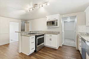 Kitchen with white cabinets, appliances with stainless steel finishes, dark hardwood / wood-style floors, and kitchen peninsula