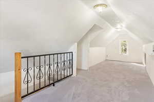 Additional living space with light colored carpet, a textured ceiling, and vaulted ceiling