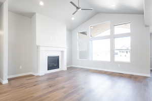 Unfurnished living room featuring ceiling fan, high vaulted ceiling, a tiled fireplace, and hardwood / wood-style floors