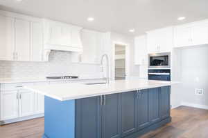 Kitchen with white cabinetry, an island with sink, light hardwood / wood-style flooring, and built in microwave