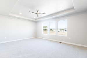 Carpeted empty room with a tray ceiling and ceiling fan