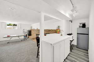 Kitchen with white cabinets, stainless steel fridge, sink, a fireplace, and a kitchen bar