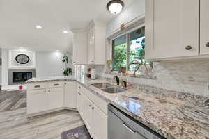 Kitchen featuring sink, kitchen peninsula, white cabinetry, dishwasher, and light wood-type flooring