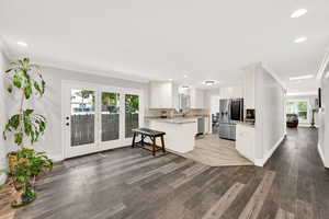 Kitchen with kitchen peninsula, tasteful backsplash, dark wood-type flooring, white cabinetry, and stainless steel appliances