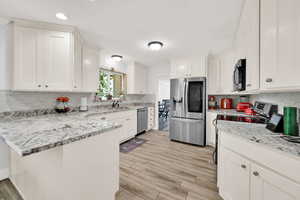 Kitchen featuring light stone counters, stainless steel appliances, light wood-type flooring, and white cabinetry