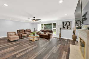 Living room featuring ceiling fan, crown molding, and dark wood-type flooring