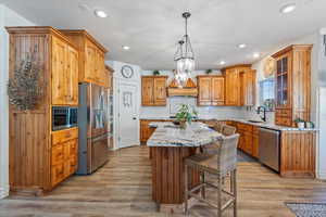 Kitchen with pendant lighting, Custom cabinetry, light hardwood / wood-style floors, appliances with stainless steel finishes, and a kitchen island, granite countertops.