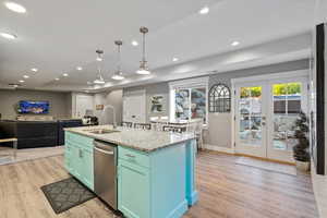 Kitchen with light wood-type flooring, stainless steel dishwasher, sink, and an island with sink