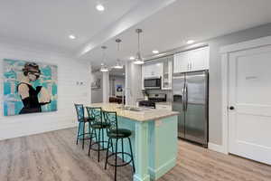 Kitchen featuring a kitchen island with sink, sink, white cabinetry, hanging light fixtures, and appliances with stainless steel finishes