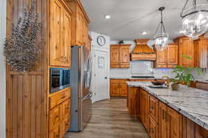 Kitchen with custom range hood, light stone counters, stainless steel appliances, light wood-type flooring, and sink