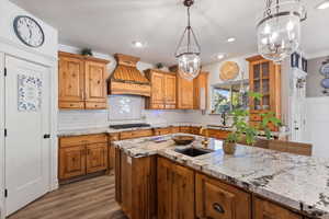 Kitchen featuring a notable chandelier, Custom cabinetry, custom exhaust hood, light hardwood / wood-style floors, and sink, granite countertops.