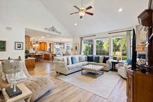 Living room with high vaulted ceiling, ceiling fan with notable chandelier, and light hardwood / wood-style flooring