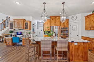 Kitchen with an island with sink, hanging light fixtures, Custom cabinetry, light hardwood / wood-style flooring, stainless steel appliances, and an granite countertops.