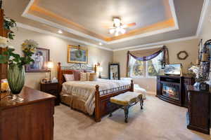 Carpeted bedroom with ceiling fan, a tray ceiling, and crown molding