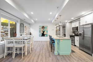 Kitchen with sink, a center island with sink, white cabinetry, appliances with stainless steel finishes, and a breakfast bar area