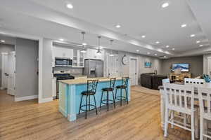 Kitchen with appliances with stainless steel finishes, white cabinets, a kitchen bar, decorative light fixtures, and a center island with sink