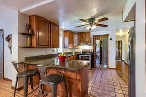 Kitchen featuring kitchen peninsula, light tile patterned floors, stainless steel appliances, stacked washer / dryer, and a textured ceiling