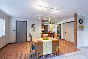 Tiled dining room with a textured ceiling, rail lighting, and ceiling fan