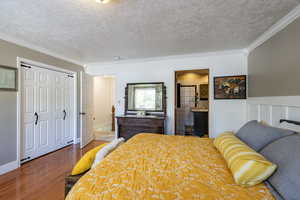 Bedroom featuring ornamental molding, hardwood / wood-style flooring, ensuite bathroom, and a textured ceiling