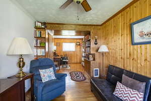 Living room with ceiling fan, wood walls, a textured ceiling, hardwood / wood-style flooring, and crown molding