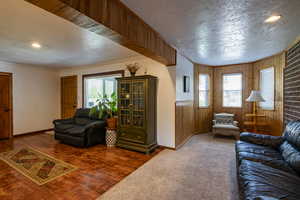 Living room featuring wood-type flooring, a textured ceiling, wooden walls, and crown molding