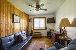 Living room featuring a textured ceiling, hardwood / wood-style flooring, wood walls, crown molding, and ceiling fan