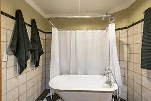 Bathroom with tile walls, tile patterned flooring, ornamental molding, and separate shower and tub