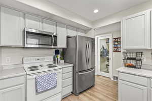 Kitchen with a textured ceiling, light hardwood / wood-style floors, white cabinetry, and stainless steel appliances