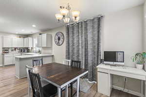 Dining space featuring an inviting chandelier, light wood-type flooring, sink, and a textured ceiling