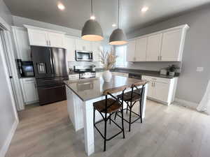 Kitchen featuring pendant lighting, a breakfast bar, a center island, white cabinetry, and stainless steel appliances