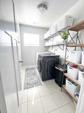 Clothes washing area featuring a textured ceiling, washer and dryer, and light tile patterned floors