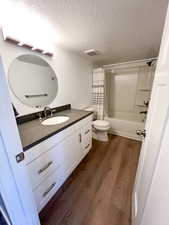 Full bathroom featuring shower / tub combo, vanity, a textured ceiling, wood-type flooring, and toilet