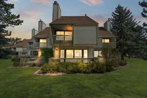 Back house at dusk with a lawn and a balcony