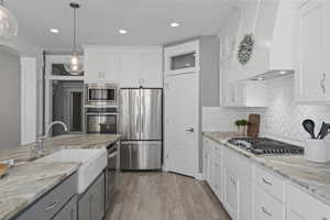 Kitchen featuring stainless steel appliances, white cabinets, custom range hood, and light wood-type flooring