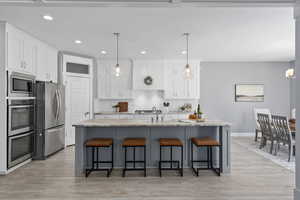 Kitchen with decorative light fixtures, a kitchen island with sink, light hardwood / wood-style flooring, white cabinetry, and appliances with stainless steel finishes