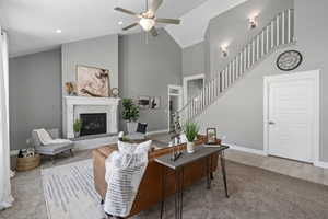 Living room featuring ceiling fan, a fireplace, carpet, and high vaulted ceiling