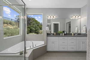 Bathroom featuring tile patterned flooring, a wealth of natural light, a relaxing tiled tub, and vanity